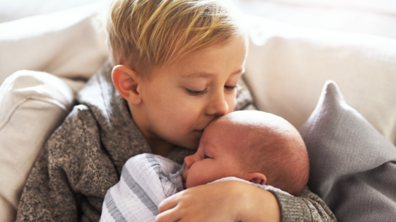 großer Bruder hält liebevoll Geschwister-Säugling