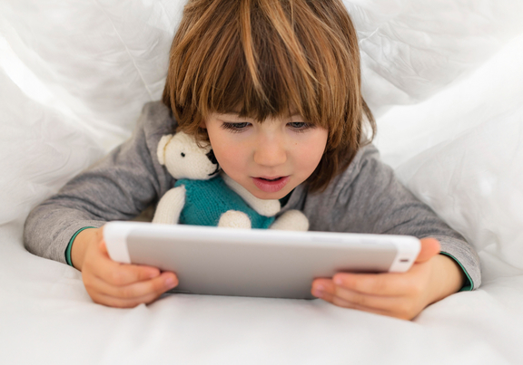 Kind was über Tablet gebeugt da sitzt