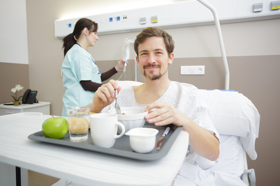 Mann im Krankenhausbett vor Tablett mit Essen